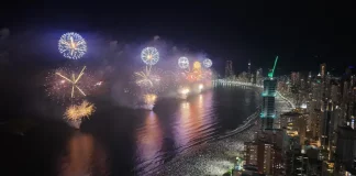Imagem aérea do Réveillon em Balneário Camboriú, mostrando a queima de fogos sobre a Praia Central lotada e a orla iluminada durante a virada do ano.