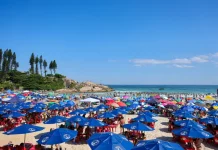 Imagem ilustra dia de calor intenso no litoral de Santa Catarina, com praia lotada, guarda-sóis abertos e grande concentração de pessoas aproveitando o tempo firme.