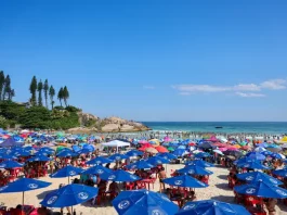 Imagem ilustra dia de calor intenso no litoral de Santa Catarina, com praia lotada, guarda-sóis abertos e grande concentração de pessoas aproveitando o tempo firme.