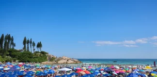 Imagem ilustra dia de calor intenso no litoral de Santa Catarina, com praia lotada, guarda-sóis abertos e grande concentração de pessoas aproveitando o tempo firme.