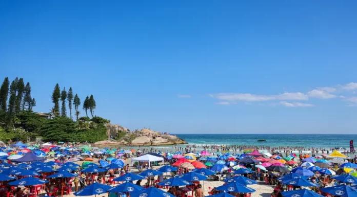 Imagem ilustra dia de calor intenso no litoral de Santa Catarina, com praia lotada, guarda-sóis abertos e grande concentração de pessoas aproveitando o tempo firme.
