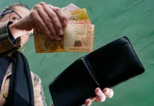 Pessoa retira cédulas de real da carteira, representando o comércio aquecido, a geração de renda e o consumo das famílias.