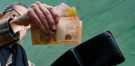 Pessoa retira cédulas de real da carteira, representando o comércio aquecido, a geração de renda e o consumo das famílias.