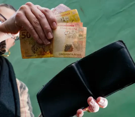 Pessoa retira cédulas de real da carteira, representando o comércio aquecido, a geração de renda e o consumo das famílias.