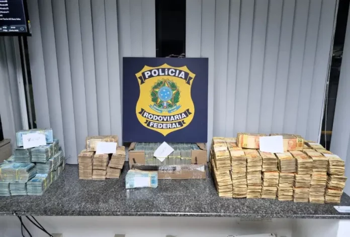 Dinheiro em espécie apreendido em ocorrência na BR-101 organizado sobre mesa, durante ação em que a PRF apreende R$ 2 milhões na rodovia.