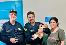 Policiais rodoviários seguram bebê ao lado da mãe após PRF salvar bebê engasgada na BR-101, em Barra Velha (SC).