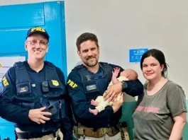 Policiais rodoviários seguram bebê ao lado da mãe após PRF salvar bebê engasgada na BR-101, em Barra Velha (SC).