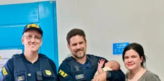 Policiais rodoviários seguram bebê ao lado da mãe após PRF salvar bebê engasgada na BR-101, em Barra Velha (SC).