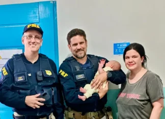 Policiais rodoviários seguram bebê ao lado da mãe após PRF salvar bebê engasgada na BR-101, em Barra Velha (SC).