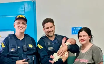 Policiais rodoviários seguram bebê ao lado da mãe após PRF salvar bebê engasgada na BR-101, em Barra Velha (SC).
