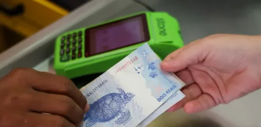 Pessoa realiza pagamento em dinheiro diante de máquina de cartão, imagem que representa acesso a crédito facilitado por programas como Pronampe SC e Juro Zero