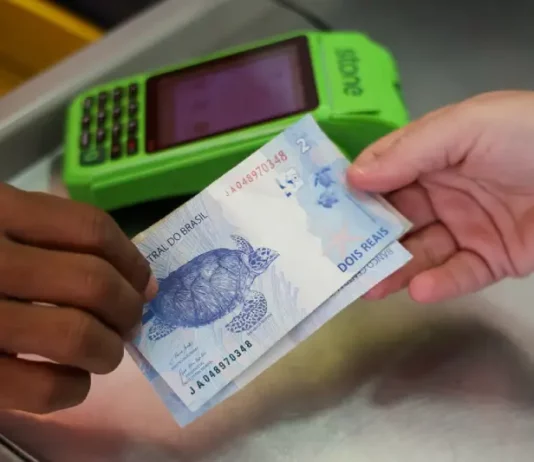 Pronampe SC e Juro Zero ajudam empreendedor a enfrentar taxas de juros elevadas Pessoa realiza pagamento em dinheiro diante de máquina de cartão, imagem que representa acesso a crédito facilitado por programas como Pronampe SC e Juro Zero