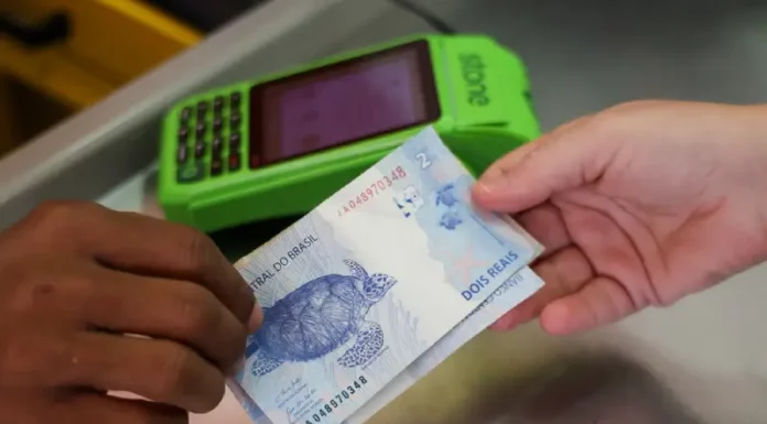 Pessoa realiza pagamento em dinheiro diante de máquina de cartão, imagem que representa acesso a crédito facilitado por programas como Pronampe SC e Juro Zero