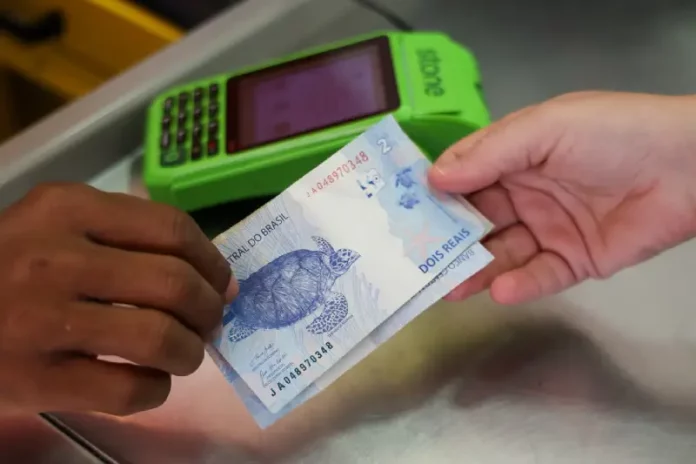 Pessoa realiza pagamento em dinheiro diante de máquina de cartão, imagem que representa acesso a crédito facilitado por programas como Pronampe SC e Juro Zero