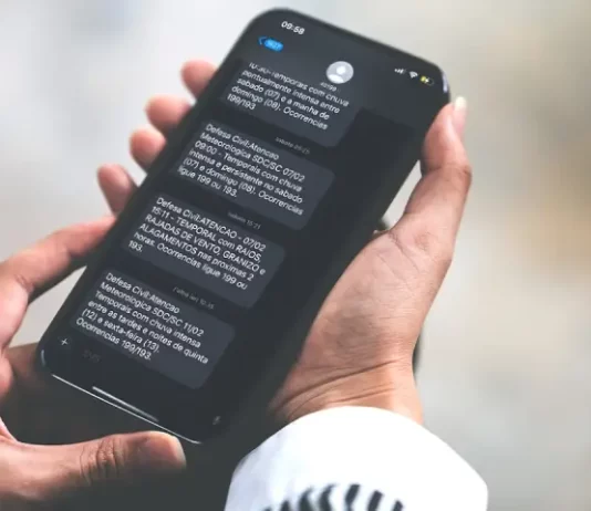 Santa Catarina tem a maior adesão nacional ao SMS de alertas de desastres da Defesa Civil Pessoa segurando celular na mão lendo alerta via SMS da Defesa Civil