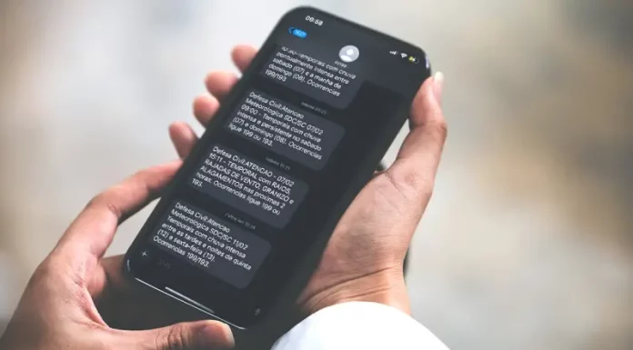 Pessoa segurando celular na mão lendo alerta via SMS da Defesa Civil