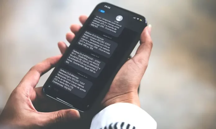 Pessoa segurando celular na mão lendo alerta via SMS da Defesa Civil