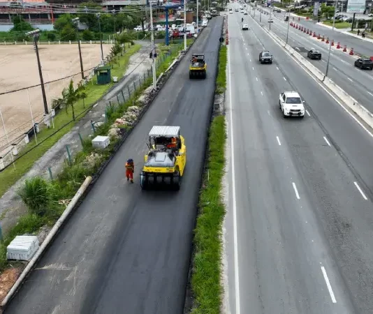 Obras de triplicação da SC-401 em Florianópolis mostram máquinas asfaltando nova faixa da rodovia, com veículos circulando nas pistas ao lado, evidenciando a ampliação da capacidade de tráfego e a melhoria da mobilidade no acesso ao Norte da Ilha.