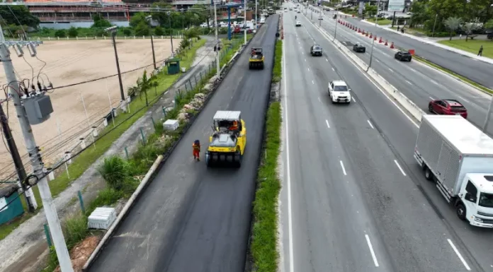 Obras de triplicação da SC-401 em Florianópolis mostram máquinas asfaltando nova faixa da rodovia, com veículos circulando nas pistas ao lado, evidenciando a ampliação da capacidade de tráfego e a melhoria da mobilidade no acesso ao Norte da Ilha.