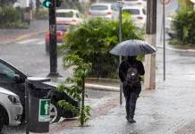 pessoa caminhando na chuva com guarda-chuva aberto, indicando a previsão do tempo de calor intenso e temporais