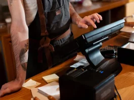 Funcionário opera o caixa no balcão de um estabelecimento, ilustrando o movimento e os desafios financeiros enfrentados pelos bares e restaurantes de Santa Catarina durante a temporada de verão.