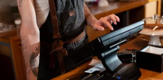 Funcionário opera o caixa no balcão de um estabelecimento, ilustrando o movimento e os desafios financeiros enfrentados pelos bares e restaurantes de Santa Catarina durante a temporada de verão.