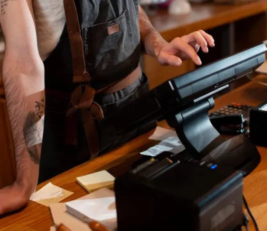 Bares e restaurantes em Santa Catarina têm verão abaixo do esperado Funcionário opera o caixa no balcão de um estabelecimento, ilustrando o movimento e os desafios financeiros enfrentados pelos bares e restaurantes de Santa Catarina durante a temporada de verão.