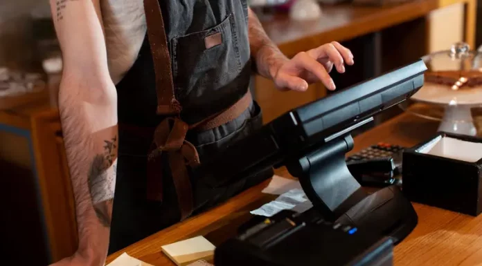 Funcionário opera o caixa no balcão de um estabelecimento, ilustrando o movimento e os desafios financeiros enfrentados pelos bares e restaurantes de Santa Catarina durante a temporada de verão.