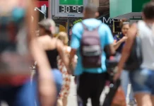 Pessoas caminham pela cidade em dia de calor em Santa Catarina, com termômetro de rua marcando 30°C ao fundo.