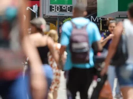 Pessoas caminham pela cidade em dia de calor em Santa Catarina, com termômetro de rua marcando 30°C ao fundo.