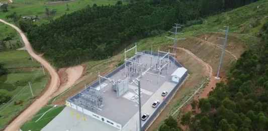 Vista aérea de uma subestação de energia elétrica instalada em área rural de Santa Catarina, cercada por vegetação e estradas de terra. A estrutura, com transformadores, torres e equipamentos de distribuição, representa os investimentos das cooperativas de energia na ampliação e modernização da rede elétrica, garantindo mais segurança energética e qualidade no fornecimento, especialmente para produtores e municípios do interior.