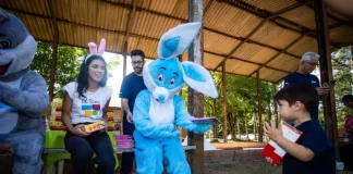 Representantes da Fundação Somar, incluindo um com fantasia de coelho, entregam chocolates a crianças, mostrando onde doar chocolate em Florianópolis durante a campanha de Páscoa.