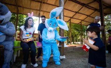Representantes da Fundação Somar, incluindo um com fantasia de coelho, entregam chocolates a crianças, mostrando onde doar chocolate em Florianópolis durante a campanha de Páscoa.