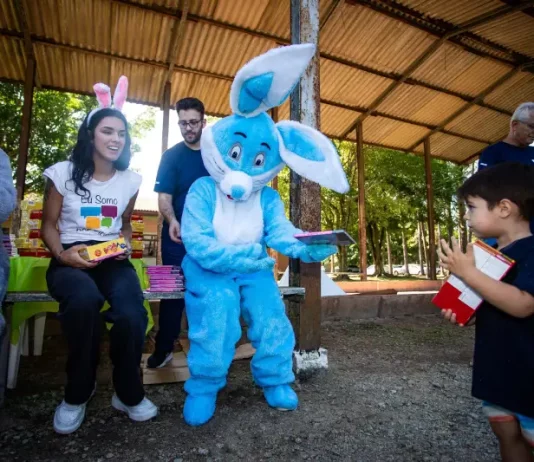 Representantes da Fundação Somar, incluindo um com fantasia de coelho, entregam chocolates a crianças, mostrando onde doar chocolate em Florianópolis durante a campanha de Páscoa.