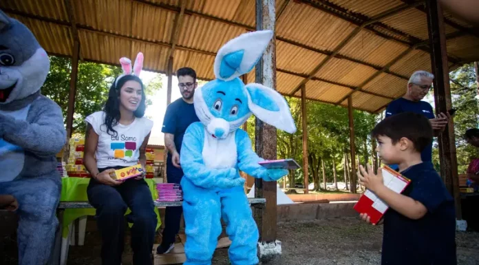 Representantes da Fundação Somar, incluindo um com fantasia de coelho, entregam chocolates a crianças, mostrando onde doar chocolate em Florianópolis durante a campanha de Páscoa.