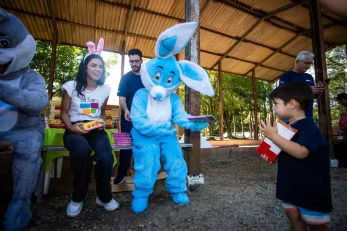 Representantes da Fundação Somar, incluindo um com fantasia de coelho, entregam chocolates a crianças, mostrando onde doar chocolate em Florianópolis durante a campanha de Páscoa.