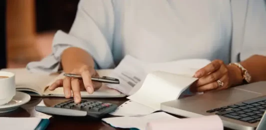 Mulher usando calculadora e revisando papéis para simbolizar a regularização de dívidas no PPI São José em Dia