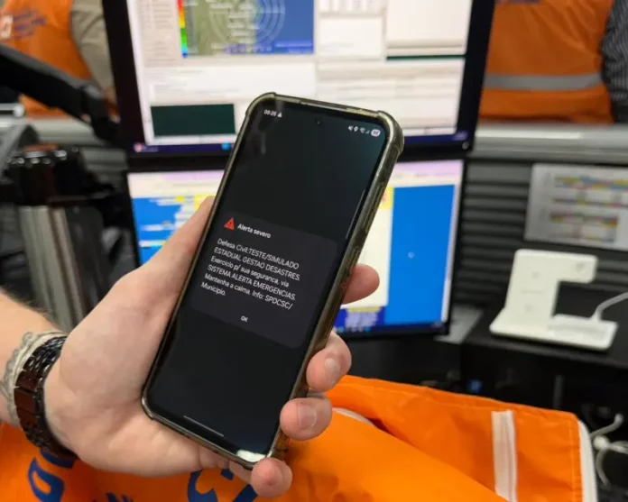 Celular exibe alerta de emergência da Defesa Civil durante simulado de desastres em Santa Catarina, demonstrando o funcionamento do sistema de avisos à população.
