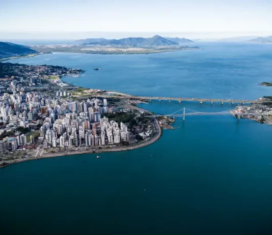 Vista aérea de Florianópolis, com destaque para a área urbana, pontes e o litoral, ilustrando o avanço da cidade em sustentabilidade por meio do programa Florianópolis Lixo Zero.