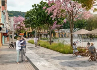 Imagem ilustrativa apresenta proposta de requalificação do Centro de Florianópolis, com calçadas amplas, ciclovia, árvores floridas e praça com fonte e mesas ao ar livre. A cena mostra pessoas caminhando, pedalando e convivendo no espaço público, ilustrando a proposta de planejamento urbano que prioriza pedestres, áreas verdes e convivência no projeto Floripa Centro.