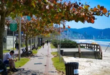 Imagem de calçadão à beira-mar em Santa Catarina, com pessoas caminhando e céu ensolarado, utilizada para ilustrar a reportagem sobre o início do outono com temperaturas acima da média, dias ainda quentes, variações térmicas ao longo do dia e a presença de instabilidades típicas da estação.