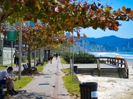 Outono em Santa Catarina terá calor acima da média e variação térmica Imagem de calçadão à beira-mar em Santa Catarina, com pessoas caminhando e céu ensolarado, utilizada para ilustrar a reportagem sobre o início do outono com temperaturas acima da média, dias ainda quentes, variações térmicas ao longo do dia e a presença de instabilidades típicas da estação.