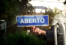Placa com a palavra “aberto” sendo colocada na porta de um estabelecimento, representando a nova oportunidade do Recupera Mais SC para regularização de dívidas de empresas e contribuintes.