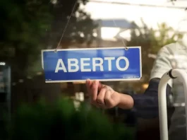 Recupera Mais SC abre renegociação de dívidas com descontos e parcelamento Placa com a palavra “aberto” sendo colocada na porta de um estabelecimento, representando a nova oportunidade do Recupera Mais SC para regularização de dívidas de empresas e contribuintes.