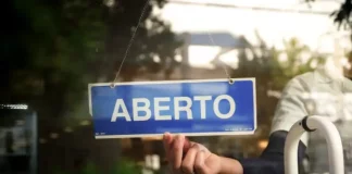 Placa com a palavra “aberto” sendo colocada na porta de um estabelecimento, representando a nova oportunidade do Recupera Mais SC para regularização de dívidas de empresas e contribuintes.