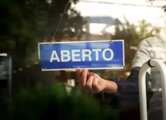 Placa com a palavra “aberto” sendo colocada na porta de um estabelecimento, representando a nova oportunidade do Recupera Mais SC para regularização de dívidas de empresas e contribuintes.