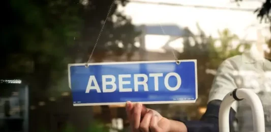 Recupera Mais SC abre renegociação de dívidas com descontos e parcelamento Placa com a palavra “aberto” sendo colocada na porta de um estabelecimento, representando a nova oportunidade do Recupera Mais SC para regularização de dívidas de empresas e contribuintes.