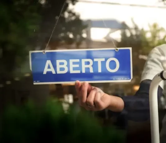Placa com a palavra “aberto” sendo colocada na porta de um estabelecimento, representando a nova oportunidade do Recupera Mais SC para regularização de dívidas de empresas e contribuintes.