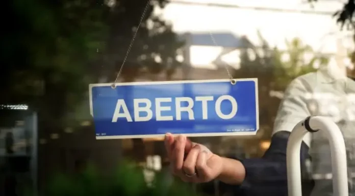 Placa com a palavra “aberto” sendo colocada na porta de um estabelecimento, representando a nova oportunidade do Recupera Mais SC para regularização de dívidas de empresas e contribuintes.