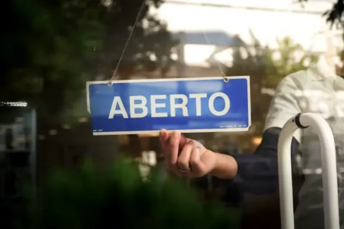 Placa com a palavra “aberto” sendo colocada na porta de um estabelecimento, representando a nova oportunidade do Recupera Mais SC para regularização de dívidas de empresas e contribuintes.
